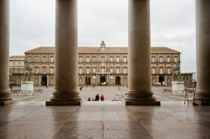 View of the Royal Palace in Naples, Italy, framed by historic columns, showcasing architectural beauty.